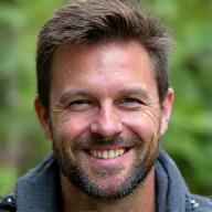 Photo de Marc Dubois, guide expert en survie, souriant dans une forêt luxuriante.